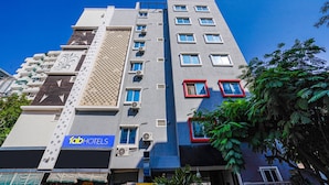 A multi-story hotel with a modern design, featuring a prominent logo on the facade, multiple air conditioning units, and a variety of window styles.