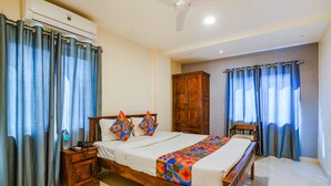 A hotel room with a wooden bed, a nightstand, an air conditioning unit, a wardrobe, and a ceiling fan.