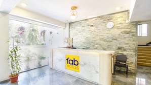 A hotel reception area with a stone wall, a reception desk, a clock, and a chair. - Fabhotel Prime Kantara (Mawal)