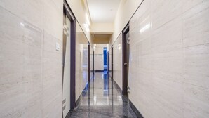 A long, narrow hallway with polished marble walls and a reflective floor, leading to a room with a blue curtain. - Fabhotel Grand Vista Inn (Bengaluru)