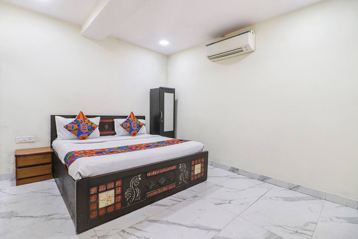 A neatly arranged bedroom with a bed, a nightstand, a wardrobe, and an air conditioning unit.