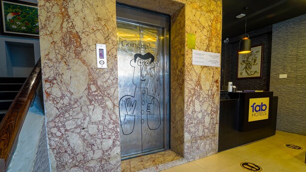 Um elevador com um personagem de desenho animado e o texto 'Subindo?' ao lado de uma mesa de recepção da Fab Hotels.