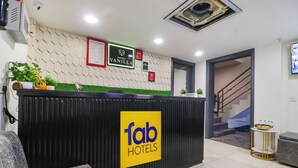 Zona de recepción de hotel con un mostrador negro, un letrero 'fab hotels' y un letrero 'hotel vanilla', y una escalera que conduce al piso superior.
