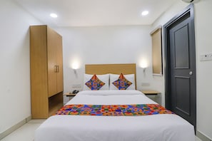 A neatly arranged bedroom with a bed, a wardrobe, a bedside table, and a door. - Fabhotel Vanilla (New Delhi)