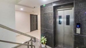 Un ascensor con pantalla digital, una planta en maceta y una puerta con una cámara de seguridad encima.