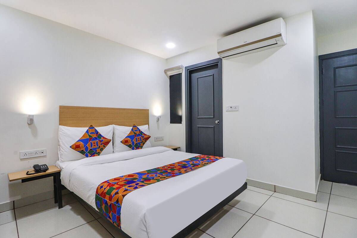 A hotel room with a bed, bedside table with a phone, two doors, and an air conditioning unit.