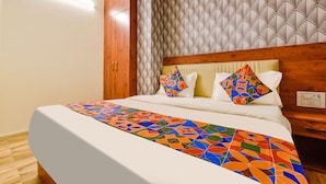 Una cama bien hecha con un colorido edredón de estampado geométrico, un cabecero de madera y un papel tapiz estampado.