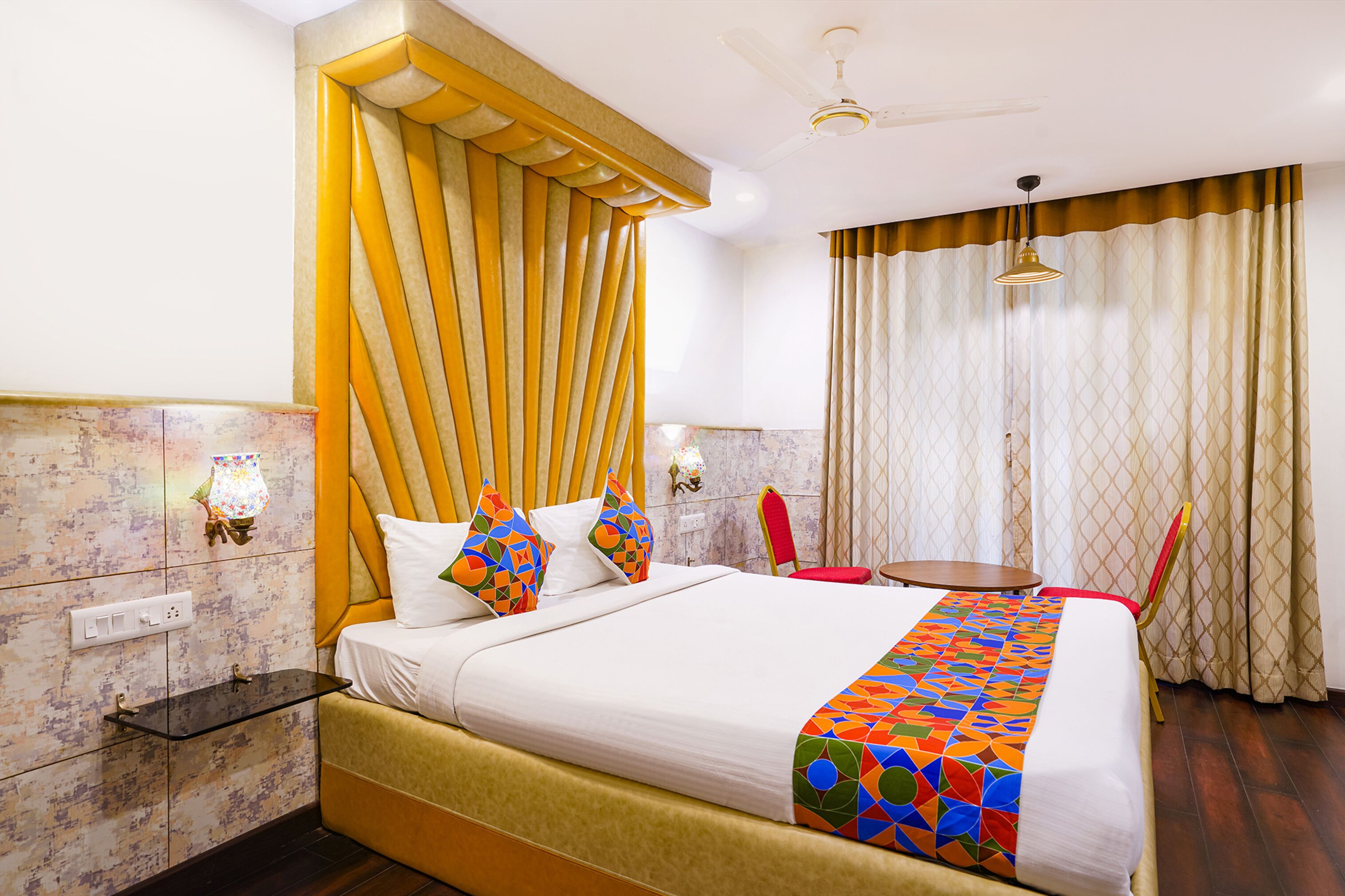 A hotel room with a large bed, a bedside table, a chair, a desk, and a window with curtains.