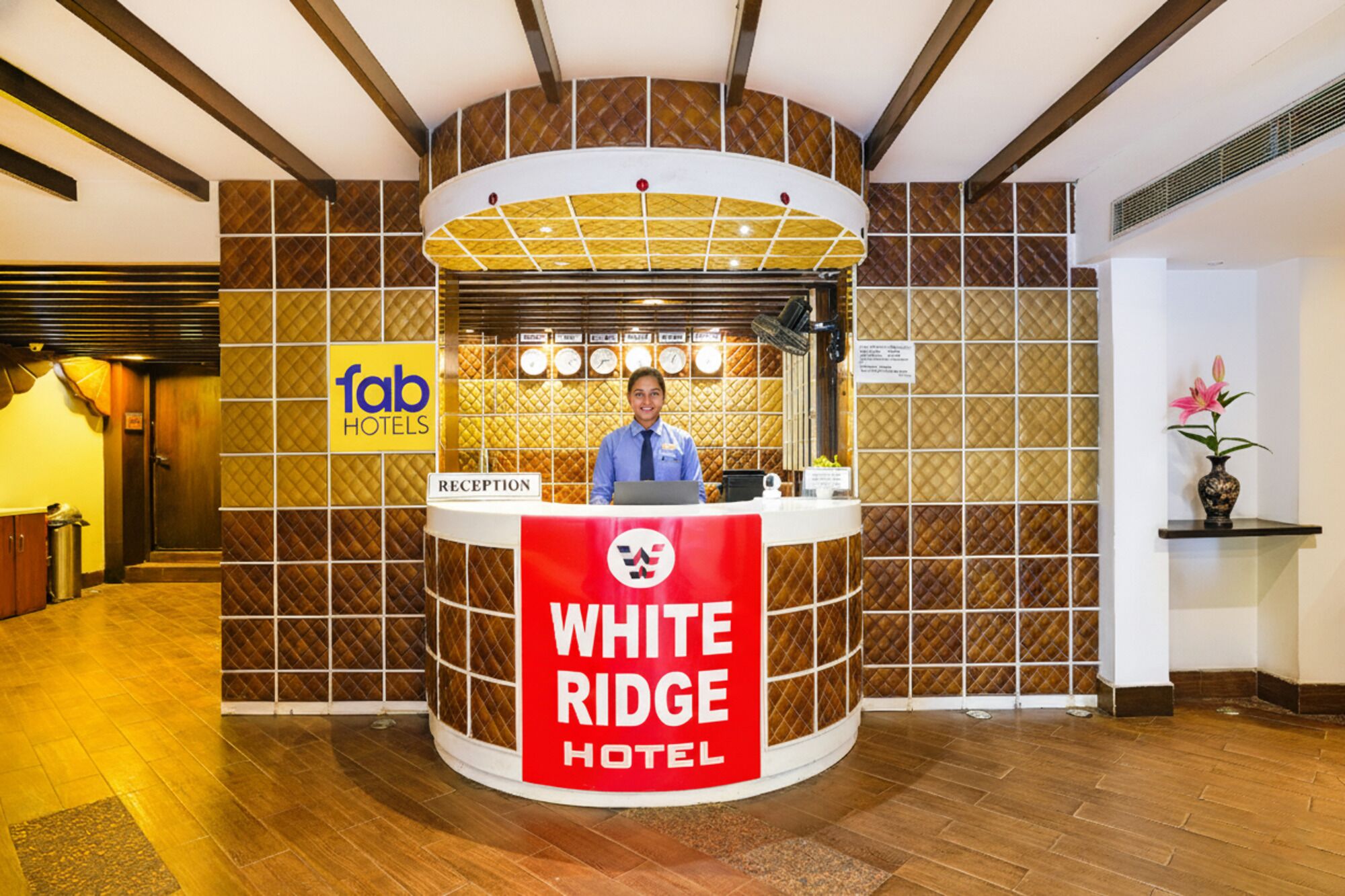 Mostrador de recepción en el Hotel White Ridge, con un miembro del personal, un reloj y un cartel de Fab Hotels.