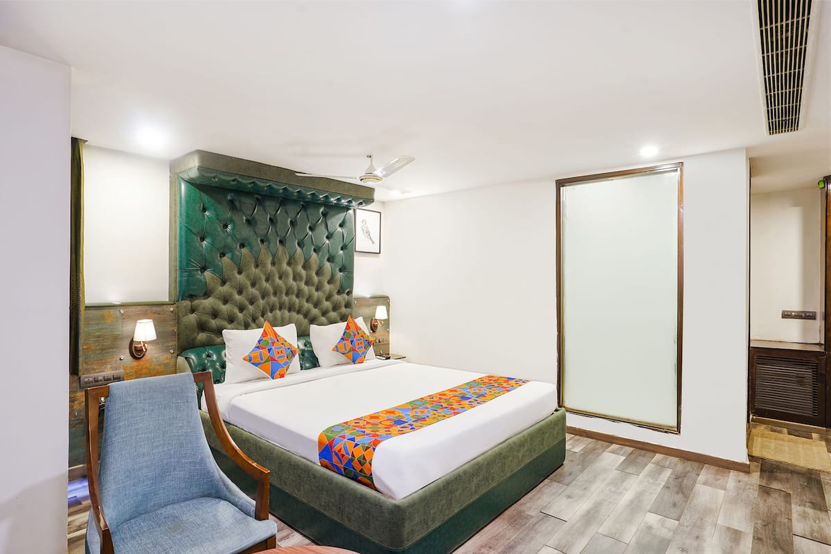Quarto de hotel com uma cama grande, cabeceira estofada, uma cadeira, mesa de cabeceira e guarda-roupa.