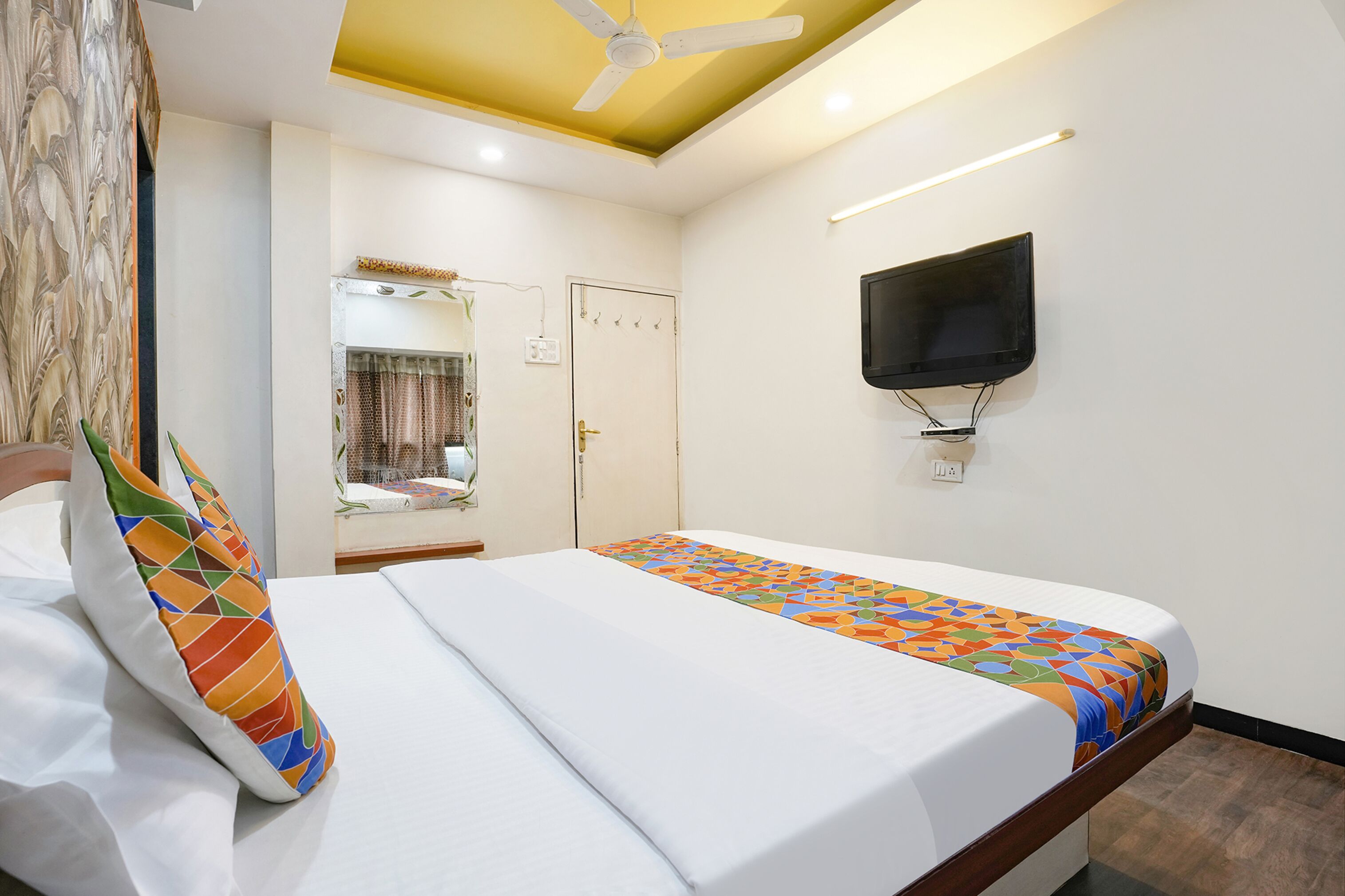 Une chambre d’hôtel avec un lit, un téléviseur fixé au mur et un ventilateur de plafond.