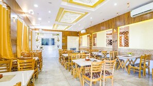 A spacious dining area with wooden tables and chairs, a central TV screen, and decorative lattice windows.