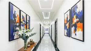 A hallway with abstract paintings on the walls, a wooden table with a vase of flowers, and a polished floor.