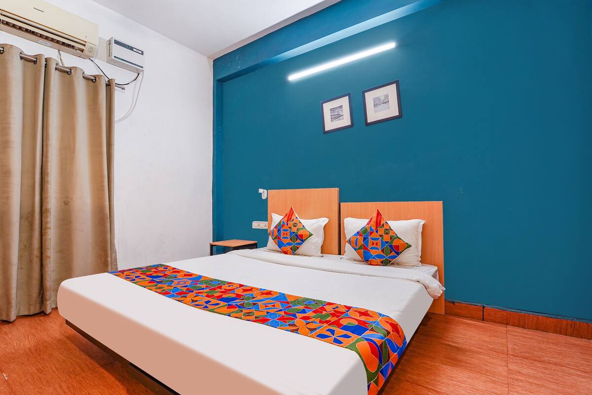 Habitación de hotel con cama, mesita de noche, aire acondicionado de pared y ventana con cortinas.