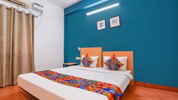 A hotel room with a bed, a nightstand, a wall-mounted air conditioner, and a window with curtains.