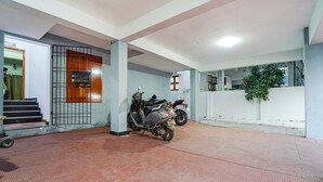 A covered parking area with two scooters parked, a staircase leading to an upper level, and a potted plant near the wall. - FabHotel Harma Residency - near Velachery Railway station (Chennai)