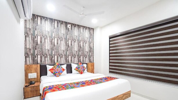 A modern bedroom with a large bed, a wooden headboard, a nightstand, and a window with blinds. - Fabhotel Prime Palace View (Vadodara)