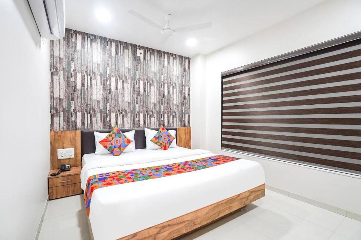 A modern bedroom with a large bed, a wooden headboard, a nightstand, and a window with blinds.