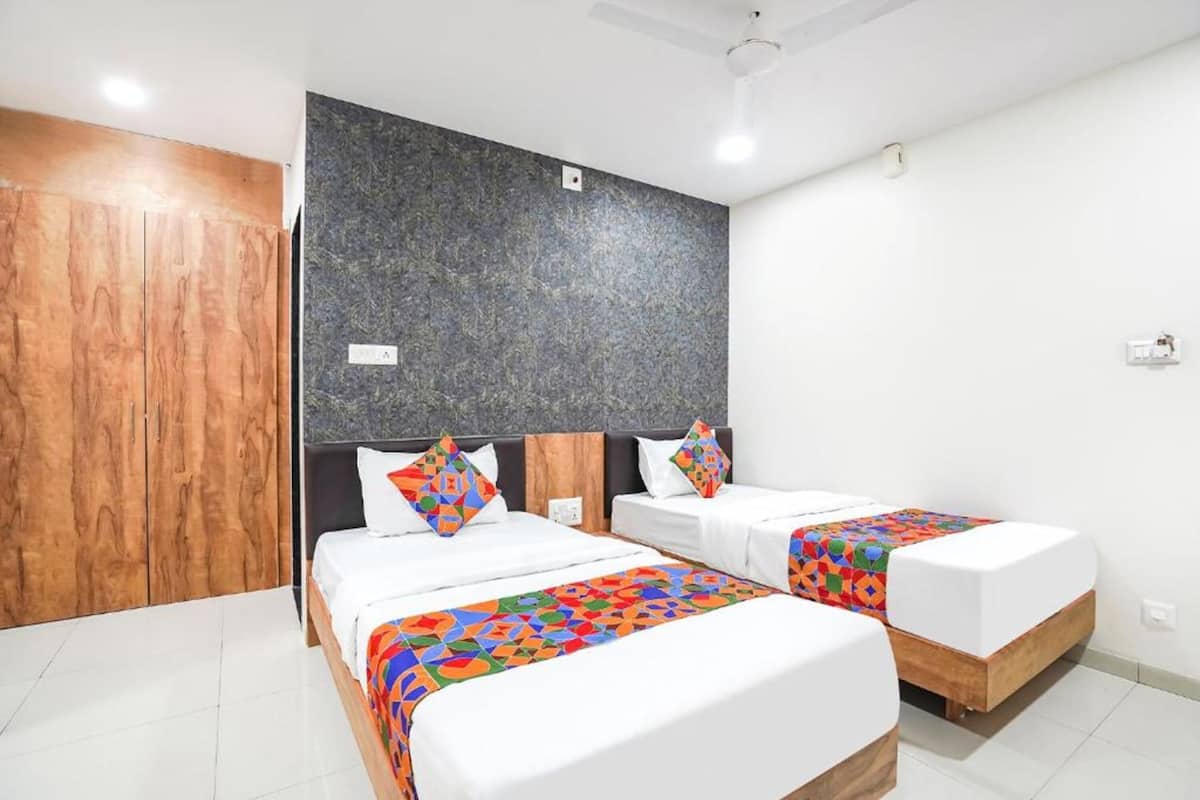 A hotel room with two beds, wooden wardrobe, grey textured wall, and white tiled floor.
