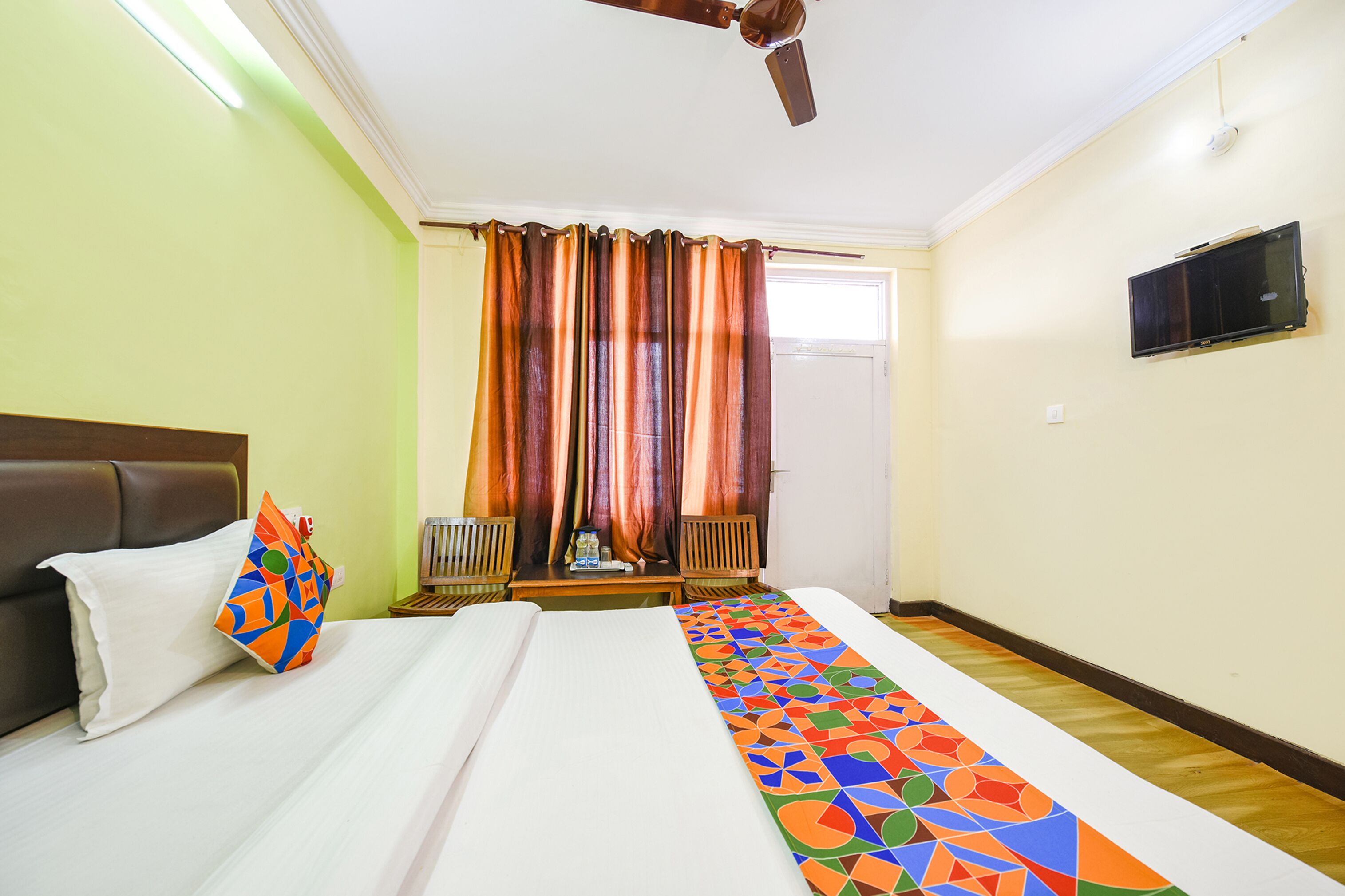 A hotel room with a bed, a ceiling fan, a television, and a window with curtains.