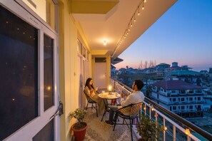 A balcony with a table and chairs, overlooking a cityscape at dusk. - Fabhotel Annapurna (Dharamshala)