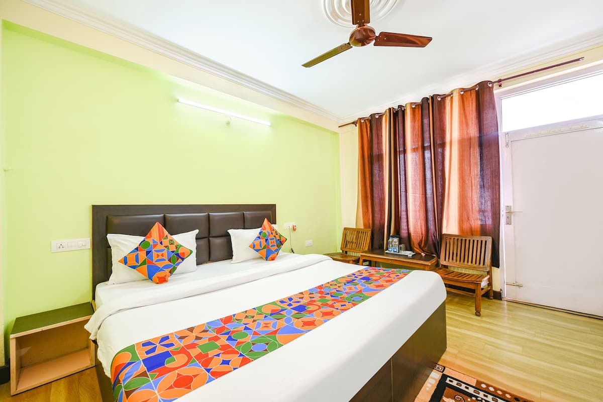 Une chambre d’hôtel avec un lit, un ventilateur de plafond, un banc en bois et une porte.