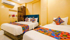 A hotel room with two beds, each with a colorful geometric-patterned bedspread, white bedding, and matching pillows. There is a wardrobe, a mirror, and a wall-mounted air conditioning unit. - Fabexpress Kurla Inn (Mumbai)