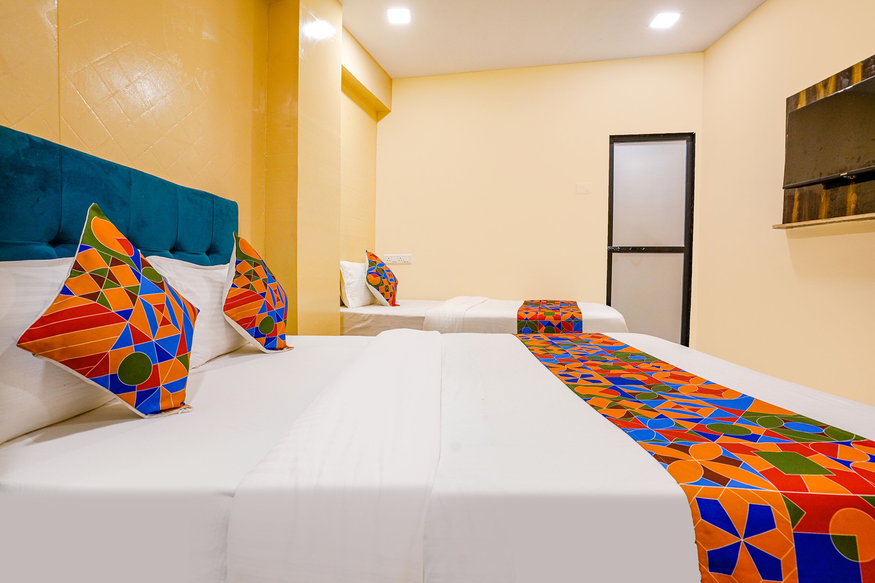 A hotel room with two beds, a blue headboard, and a colorful geometric-patterned bed runner.