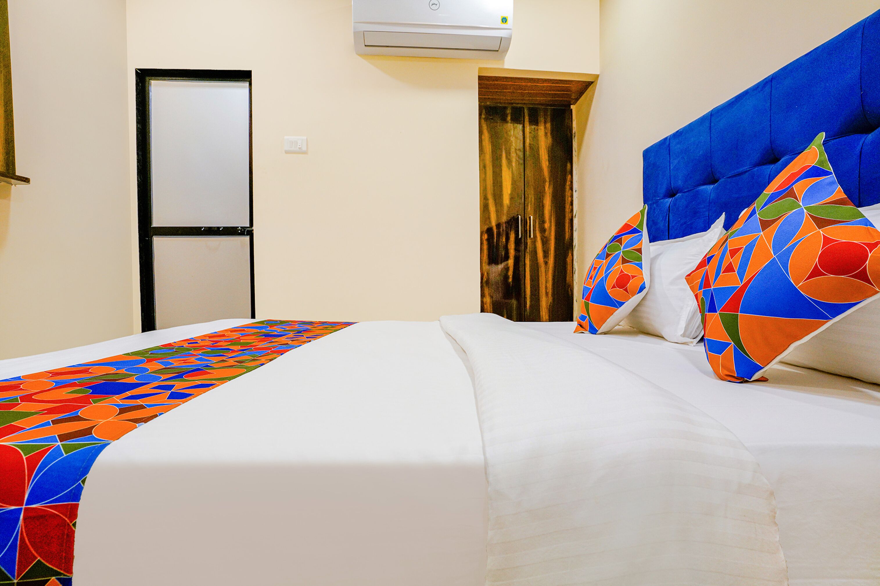 A hotel room with a bed, a door, and an air conditioning unit.