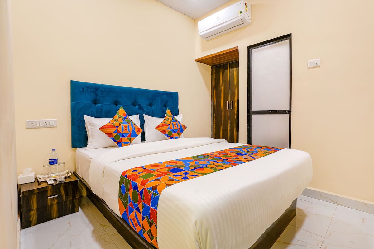 A hotel room with a large bed, a blue headboard, and a colorful bedspread.