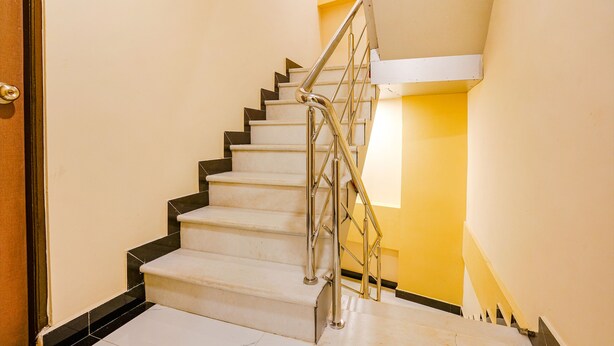 A staircase with a metal handrail and black steps, leading to a landing with a light fixture. - Fabexpress Kurla Inn (Mumbai)