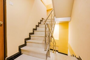 A staircase with a metal handrail and black steps, leading to a landing with a light fixture. - Fabexpress Kurla Inn (Mumbai)