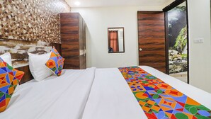 A hotel room with a large bed, a wooden headboard, a mirror, and a view of a rocky outdoor area. - Fabhotel Empire Suites (New Delhi)