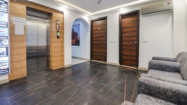 A lobby with a reception desk, a waiting area with grey sofas, a ceiling fan, and a large poster on the wall. - Fabhotel Empire Suites (New Delhi)