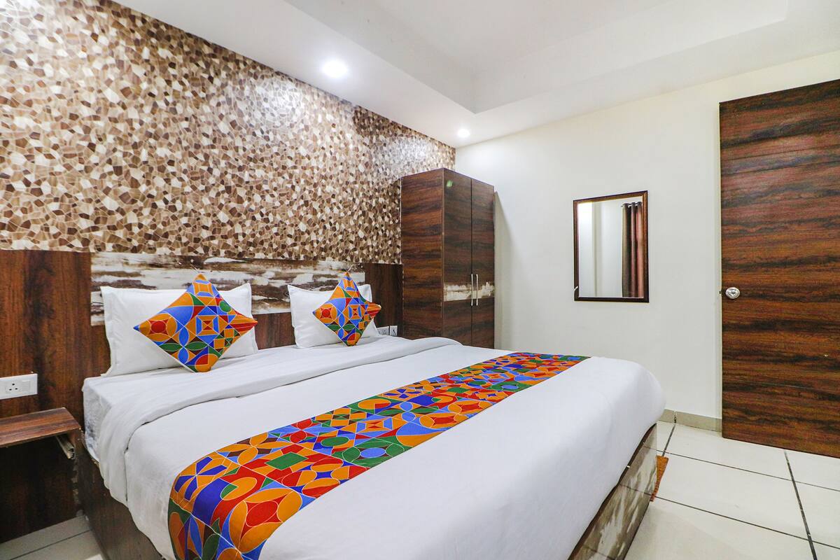 A hotel room with a bed, wooden headboard, a colorful bed runner, a wooden wardrobe, and a mirror on the wall.