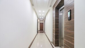 A hallway with a wooden wall, a door at the end, and a digital display on the wall. - Fabhotel Empire Suites (New Delhi)
