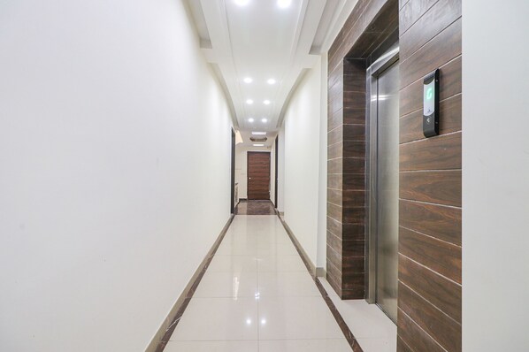 A hallway with a wooden wall, a door at the end, and a digital display on the wall. - Fabhotel Empire Suites (New Delhi)