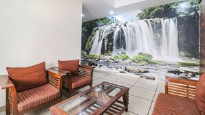 A room with a waterfall mural, wooden furniture, and a glass coffee table. - Fabhotel Empire Suites (New Delhi)