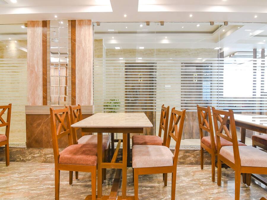 Comedor con mesas y sillas de madera, suelo de mármol y un separador de vidrio con panel de madera.