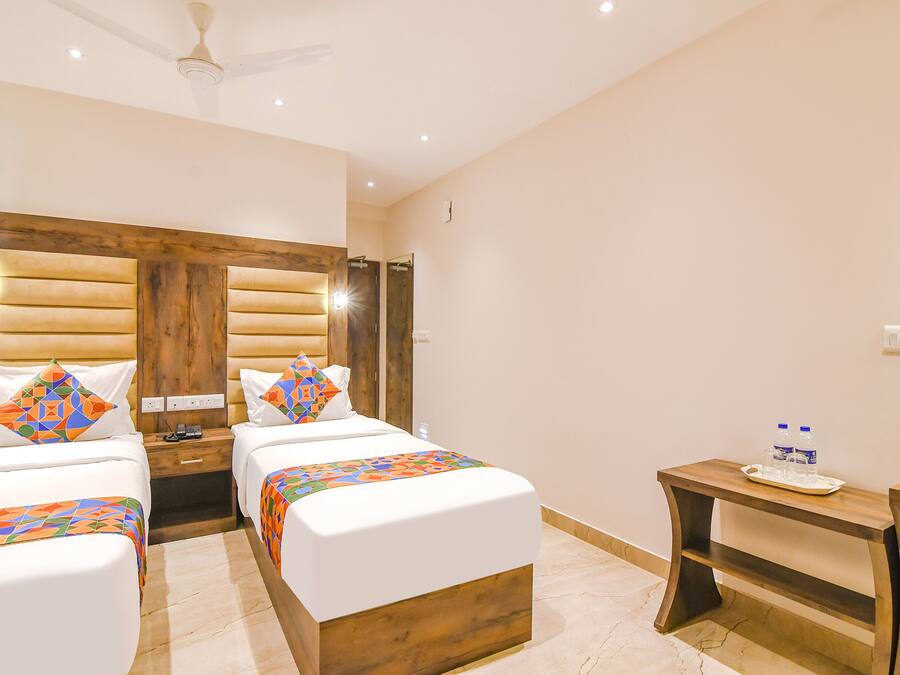 Habitación de hotel con dos camas, cabecera de madera, una mesita con botellas de agua y un ventilador de techo.