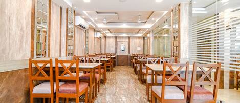 Un restaurante espacioso con mesas y sillas de madera, piso de mármol y un diseño moderno de techo.