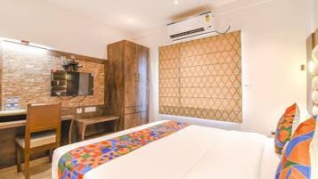 Una habitación de hotel con cama, un escritorio con silla, un televisor montado en una pared de ladrillo y una cortina estampada.