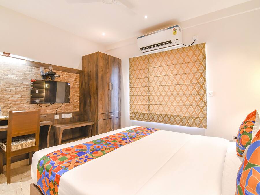 Una habitación de hotel con cama, un escritorio con silla, un televisor montado en una pared de ladrillo y una cortina estampada.
