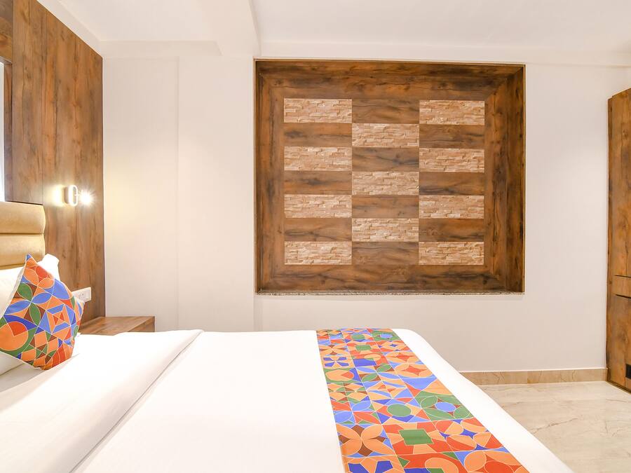 A bedroom with a bed, a colorful pillow, a wooden headboard, a wall-mounted light, and a wooden cabinet.