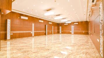 Una amplia sala de conferencias, bien iluminada, con suelo de mármol pulido, paneles de madera y luces empotradas en el techo.
