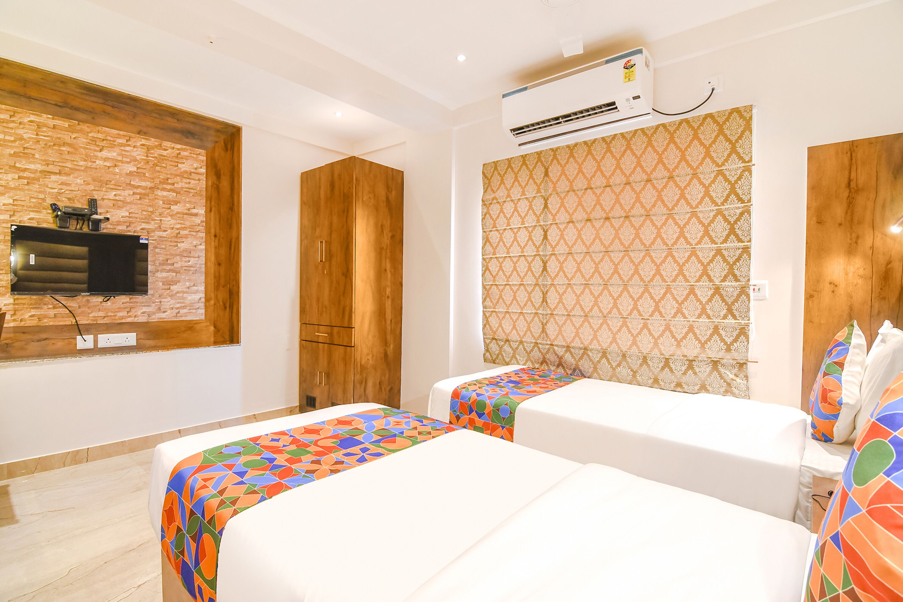 Habitación de hotel con dos camas, un televisor montado en una pared de ladrillo y un equipo de aire acondicionado.