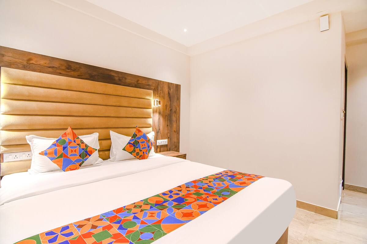 Quarto de hotel com uma cama grande, cabeceira de madeira e um cobre-leito geométrico colorido.