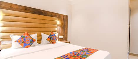 A hotel room with a large bed, wooden headboard, and a colorful geometric bed runner.
