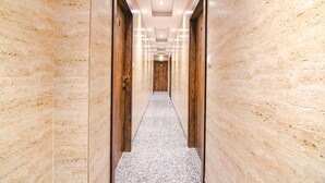 Un pasillo con paredes de mármol y suelo alfombrado, que conduce a una puerta de madera al final.