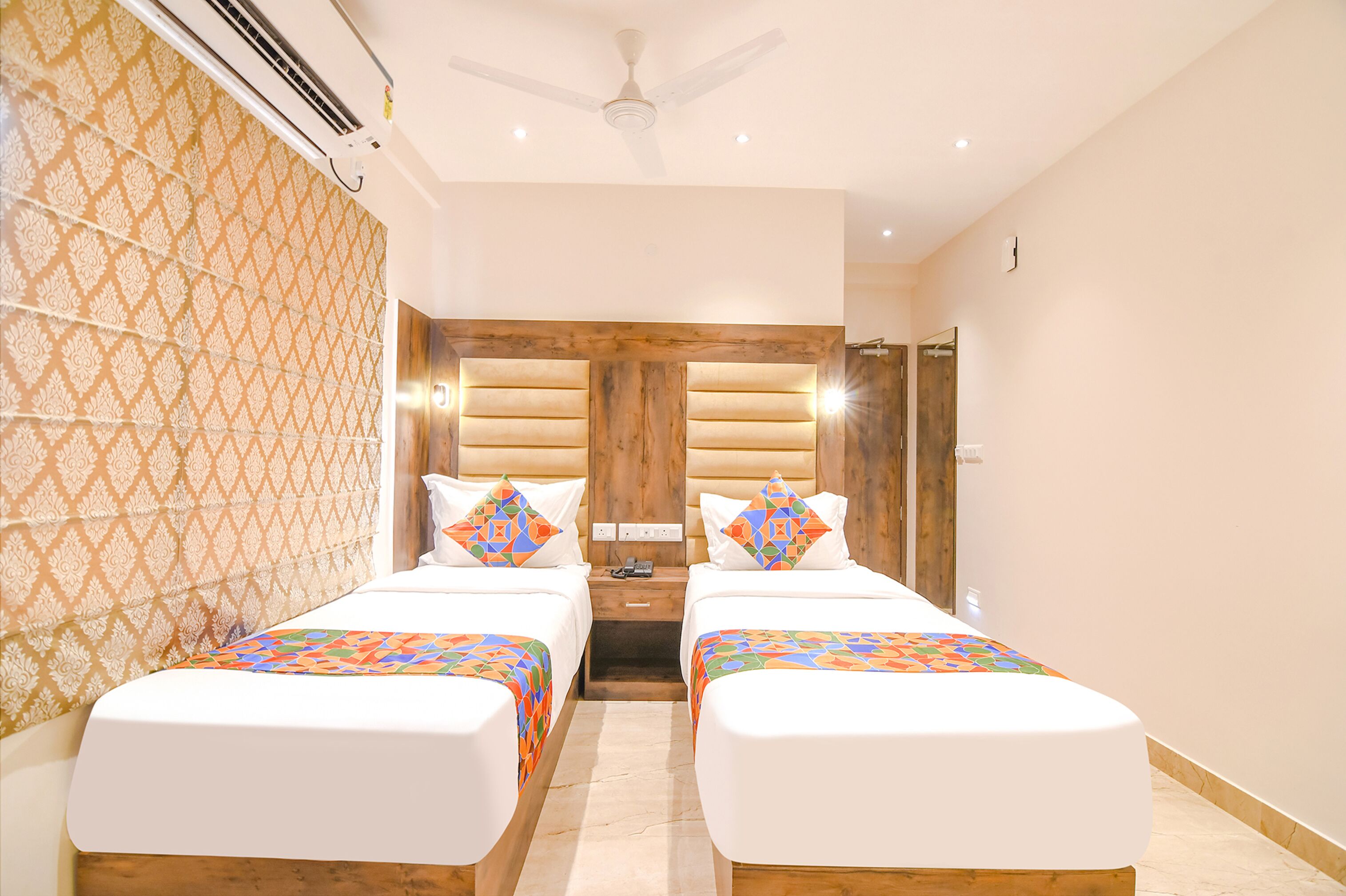 A hotel room with two beds, a wooden headboard, a ceiling fan, and a patterned wall.